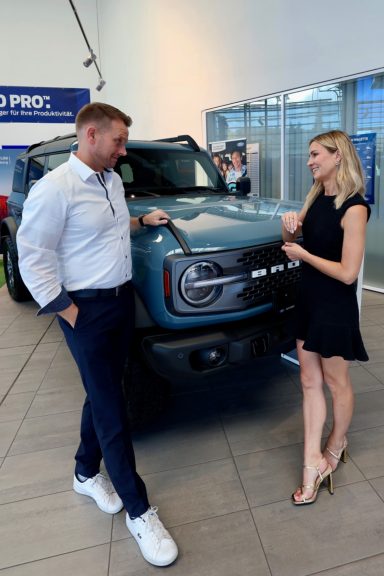 Mann und Frau stehen neben einem blauen SUV in einem modernen Ausstellungsraum.