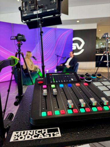 Podcast-Setup mit Mikrofonen, Kameras und einem Mischpult vor buntem Hintergrund.