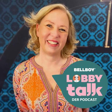 Lächelnde Frau mit blonden Haaren, bunte Bluse, vor blauem Hintergrund. Logo des Podcasts.