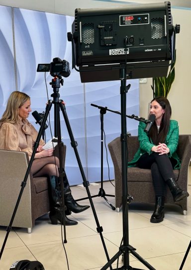 Zwei Frauen sitzen in einem Raum, eine interviewt die andere, Kameras sind aufgestellt.