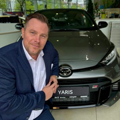 Mann im Anzug posiert neben einem grauen Toyota Yaris.