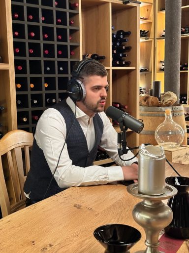 Mann mit Kopfhörern und Mikrofon sitzt an einem Tisch in einem Weinkeller.