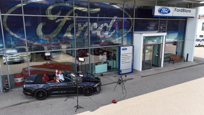 Ein Ford-Auto steht vor einem Ford-Autohaus mit Werbeschildern.
